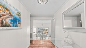 A hallway with a tiled floor, a dining area with a table and chairs, and a glass-top table with a swan sculpture.