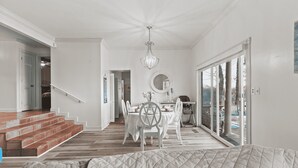 A spacious living area with a dining table and chairs, a chandelier, and a view of the outdoors through large windows.
