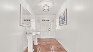 A hallway with white walls, a white door, a white pedestal sink, and a painting on the wall.