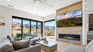 A modern living room with a large window, a fireplace, and a view of a mountainous landscape. - Panoramic Views, High End & Modern Decor, Walk To Tlaquepaque, Hot Tub (Sedona)