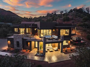 Une maison moderne à deux étages, dotée d’un patio, de grandes fenêtres et d’une façade en pierre.