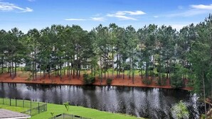 A lakeside view with a wooden dock, surrounded by dense trees and residential buildings in the background. - Savannahe Friendly Guest House (Pooler)