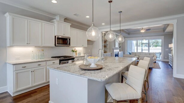 A spacious kitchen with white cabinetry, a central island with bar stools, and pendant lighting. - Savannahe Friendly Guest House (Pooler)