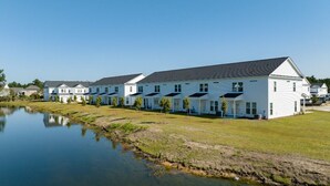 A row of white buildings with a grassy area and a body of water in front. - Savannahe Friendly Guest House (Pooler)