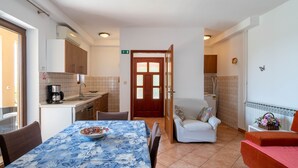 A compact kitchen with a coffee maker, a dining table with a floral tablecloth, and a sofa in the living area.