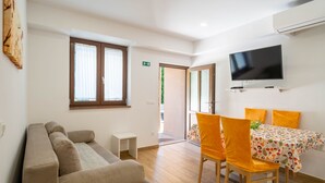 Un salon moderne comprenant un canapé, une table à manger avec des chaises, un téléviseur à écran plat et une petite table d’appoint.