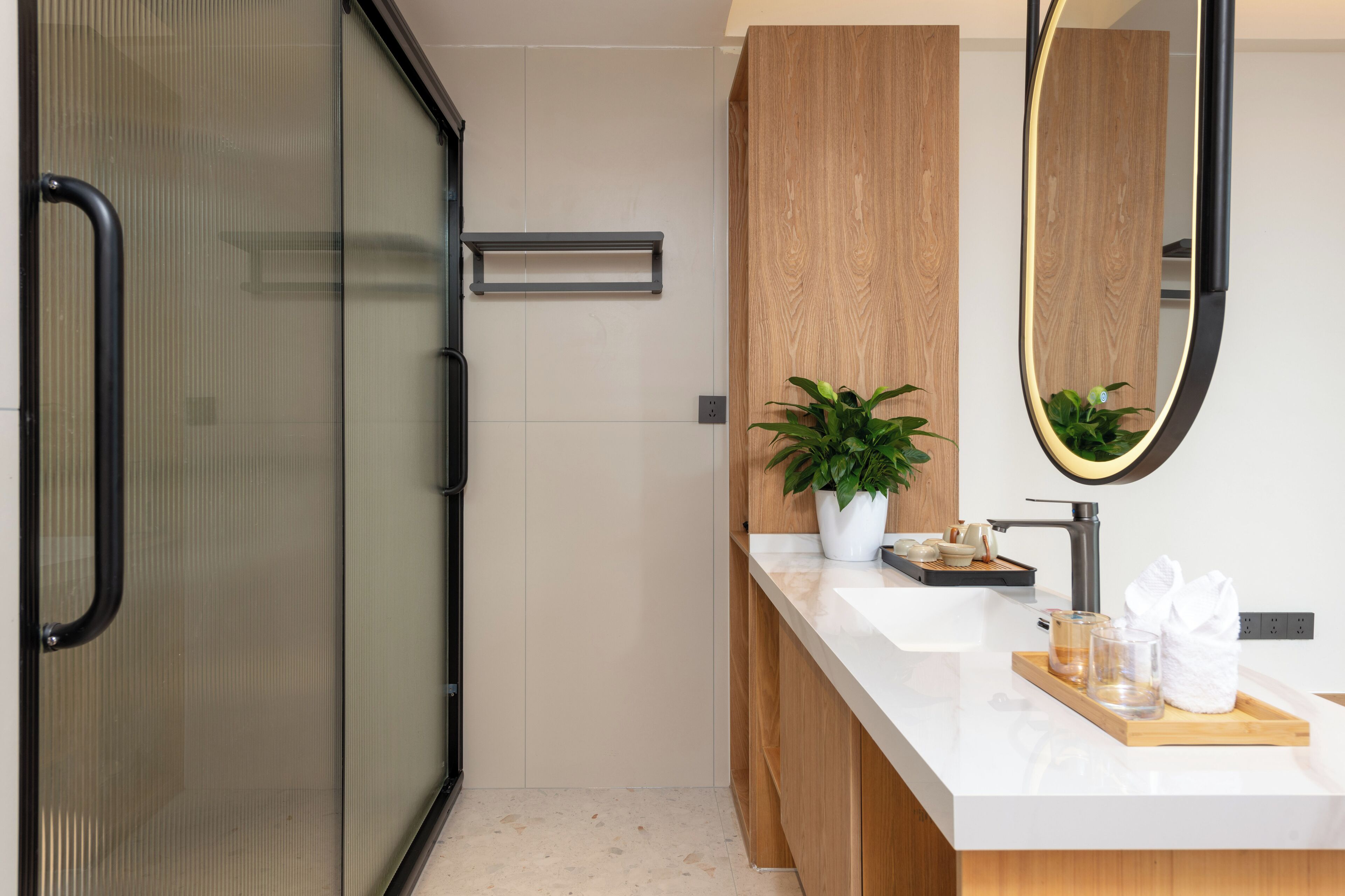 A modern bathroom with a glass shower enclosure, a wooden vanity, a large mirror, and a tray with toiletries.
