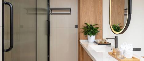 A modern bathroom with a glass shower enclosure, a wooden vanity, a large mirror, and a tray with toiletries.