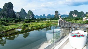 A scenic view of a river with traditional architecture, including a curved roof structure and a large white bathtub with red flowers. - Hidden Dragon Villa (Guilin)