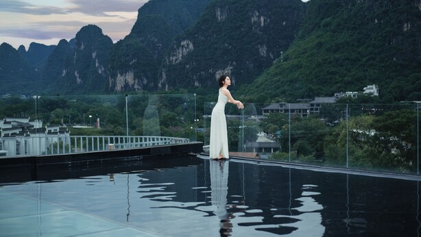 A person standing on a reflective pool with a mountainous landscape in the background. - Hidden Dragon Villa (Guilin)