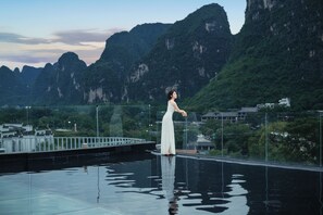 A person standing on a reflective pool with a mountainous landscape in the background. - Hidden Dragon Villa (Guilin)
