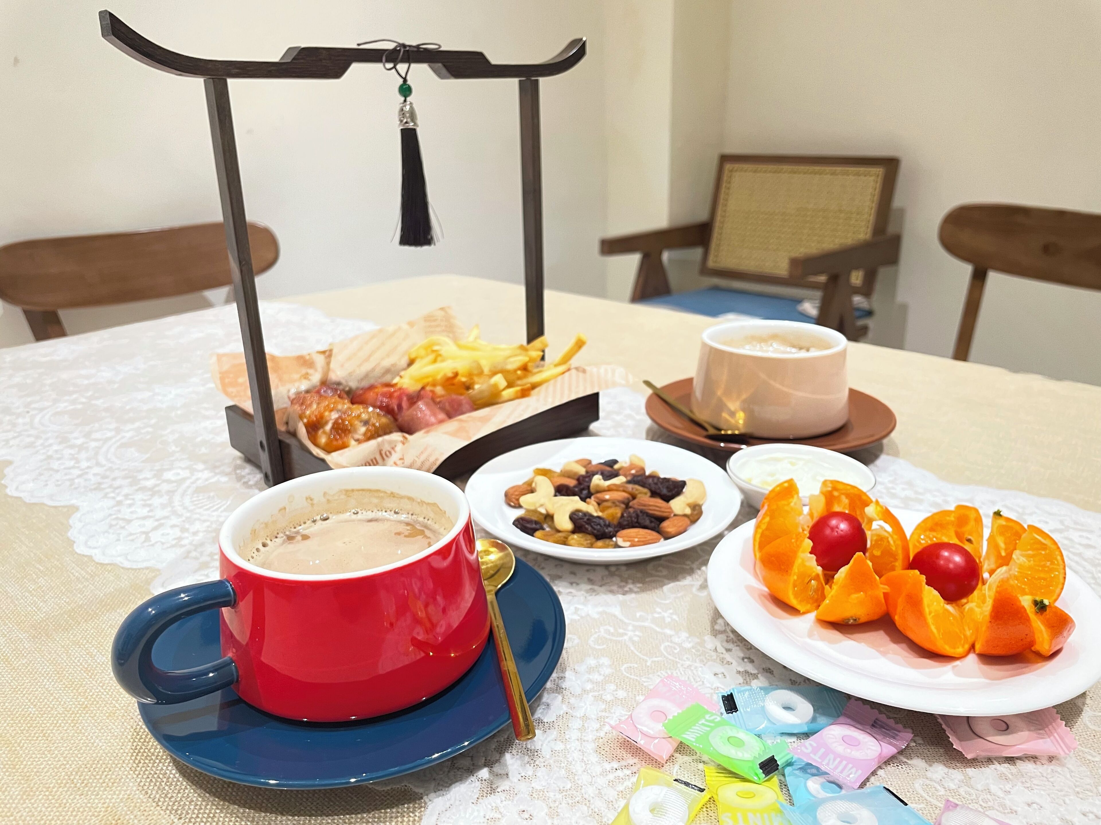 Et bord med en kaffekop, et fad med frugt, en skål med nødder, en bakke med mad og en tepotte.