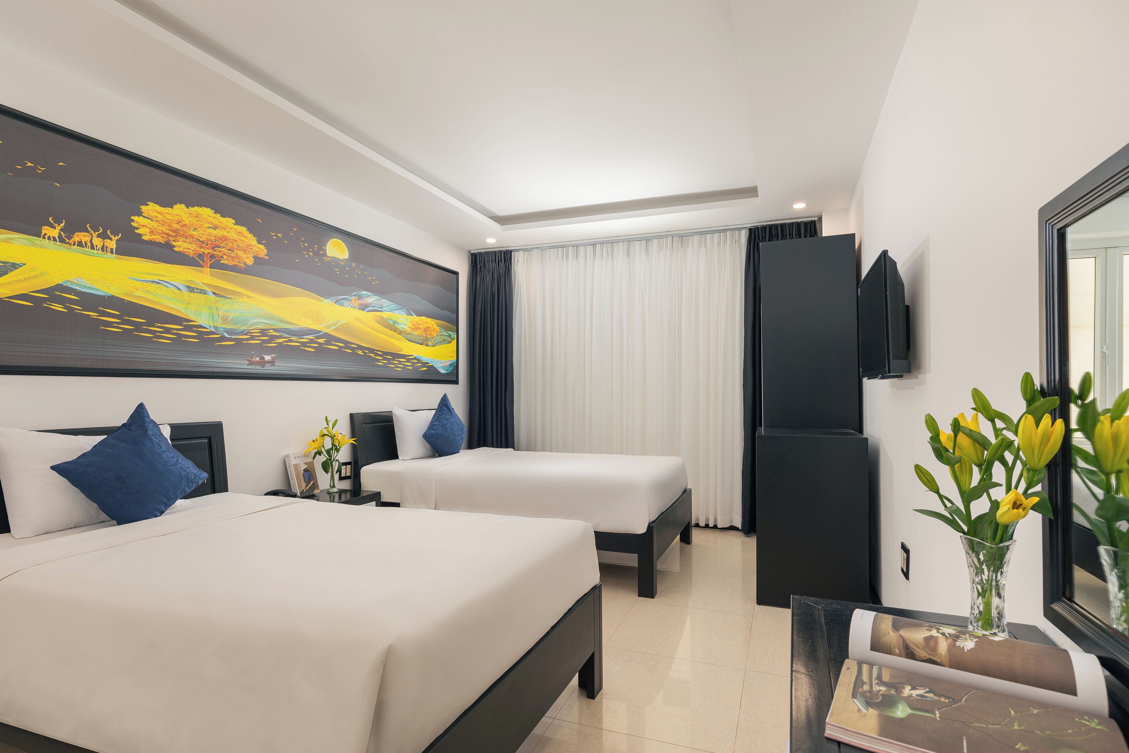Habitación de hotel con dos camas, un cuadro grande en la pared, un televisor de pantalla plana y un florero con flores sobre la mesita de noche.
