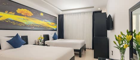 Habitación de hotel con dos camas, un cuadro grande en la pared, un televisor de pantalla plana y un florero con flores sobre la mesita de noche.