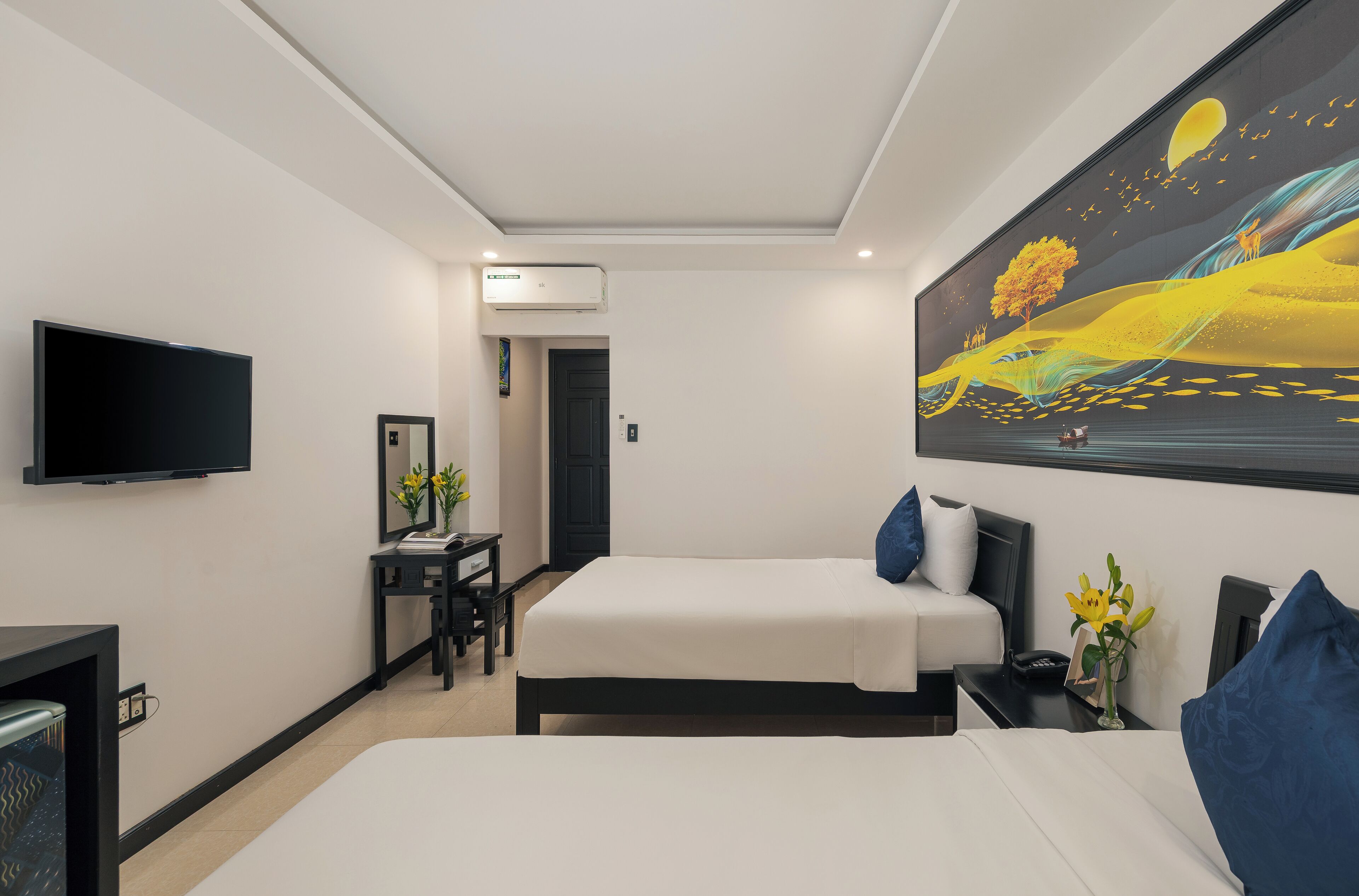 Habitación de hotel con cama, mesita de noche, televisor, escritorio, silla y un cuadro en la pared.