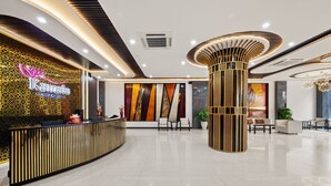 A modern hotel lobby with a reception desk, seating area, and decorative columns.
