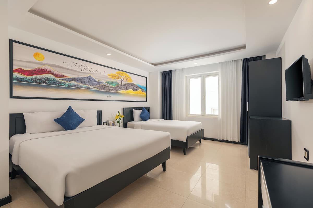 Een hotelkamer met een groot bed, een kleiner bed, een flatscreen-tv en een landschapsschilderij aan de muur.