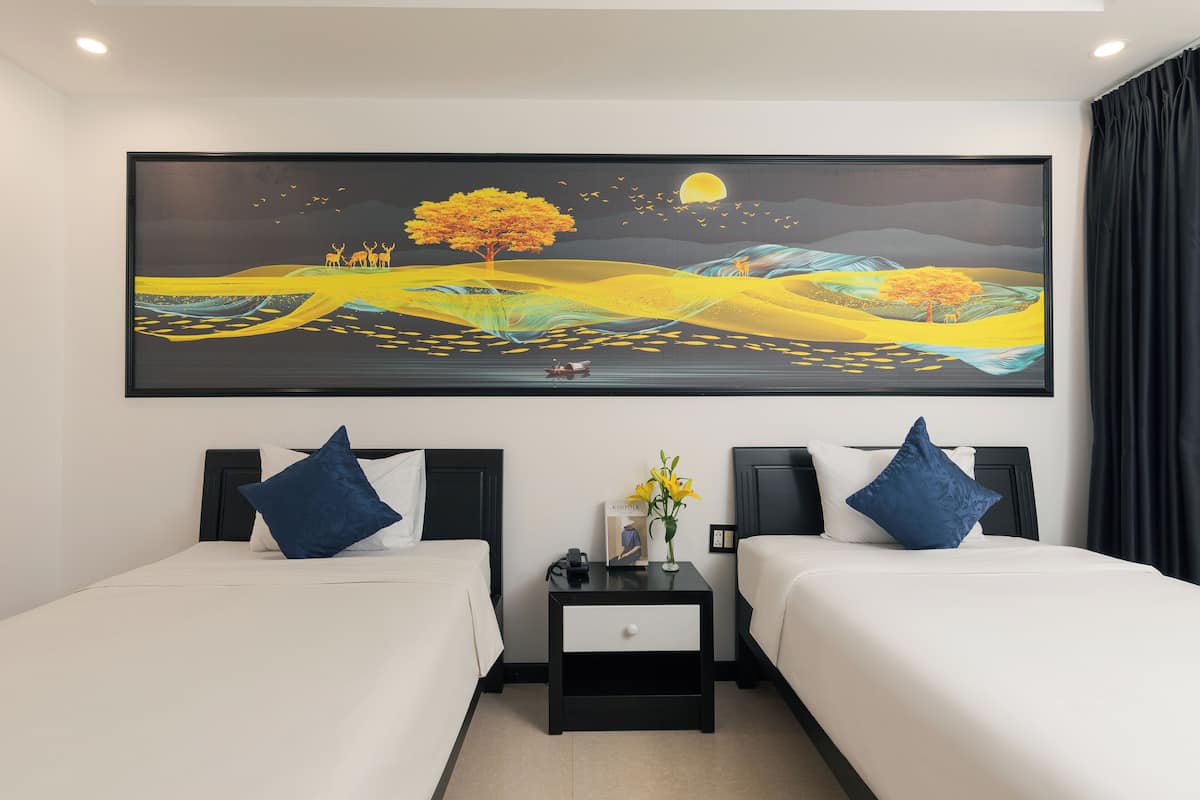 Een hotelkamer met twee bedden, een nachtkastje met een bloevas en een groot landschap op de muur.