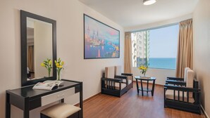 A hotel room with a desk, chair, and a view of the sea.