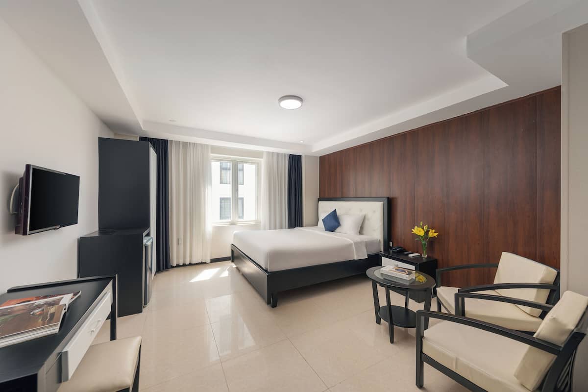 Een hotelkamer met een bed, een bureau met stoel, een televisie en een tafeltje met een bloevas.