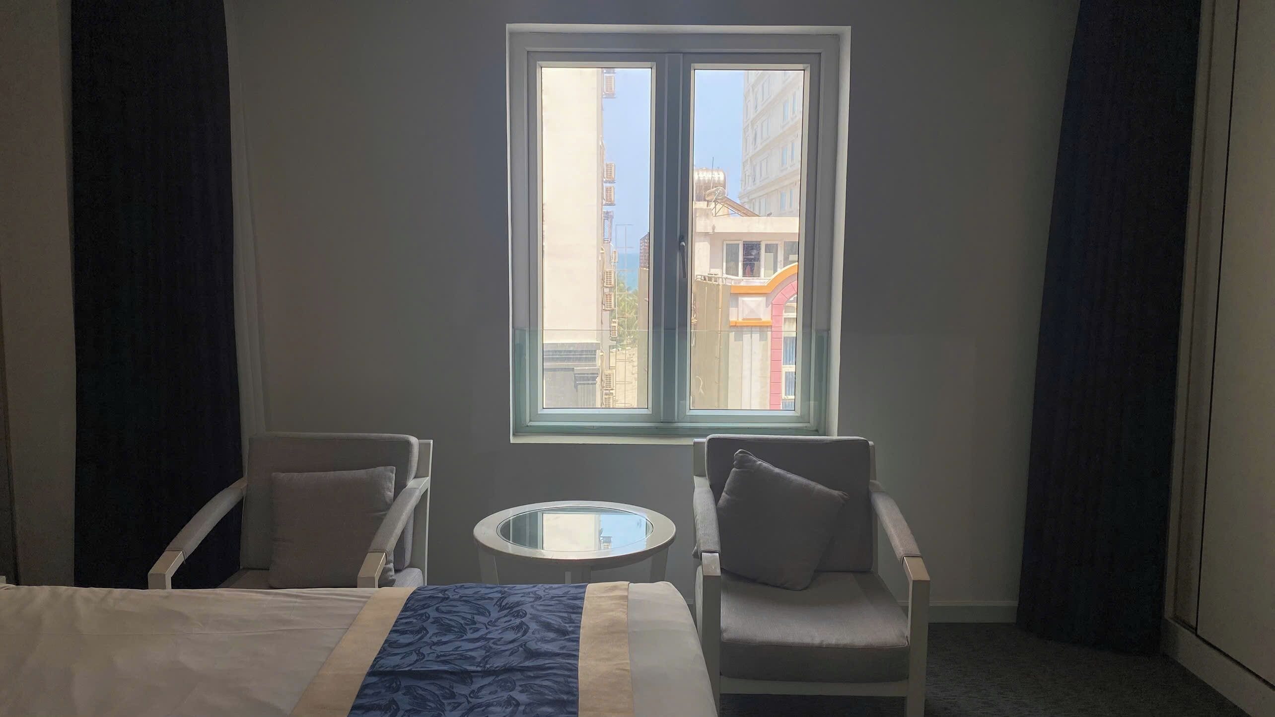 A hotel room with a bed, two armchairs, a small round table, and a window with a view of buildings.