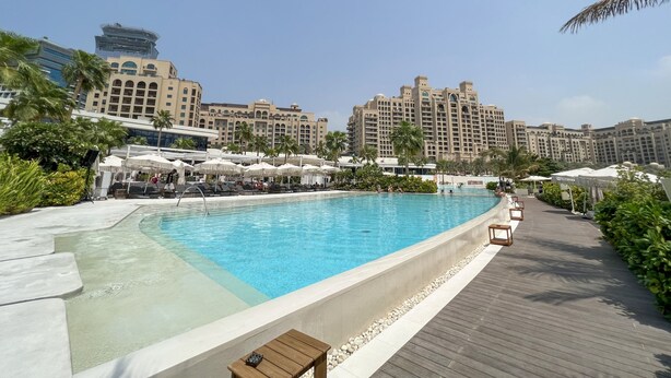 A swimming pool with lounge chairs and umbrellas, surrounded by palm trees and a large hotel building in the background. - Unit 146 Seven Palm in Dubai (Dubai)