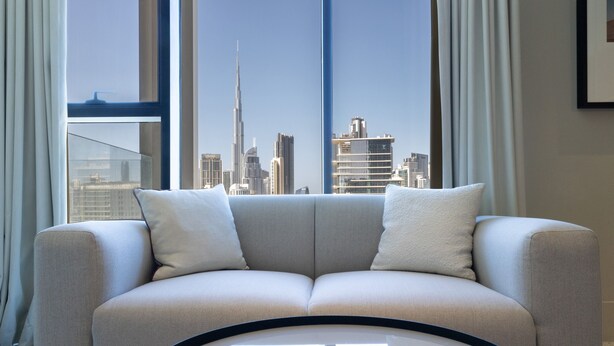 A modern living room with a sofa facing a large window offering a city skyline view. - Unit 2223 Upside Living (Dubai)
