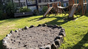 Ein Spielplatz mit Rutschen, Klettergerüsten, einem Sandkasten und einer Rasenfläche mit einer Bank.