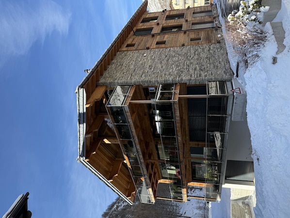 Un bâtiment moderne doté d’une façade en bois, de grandes fenêtres et d’un toit en pierre.