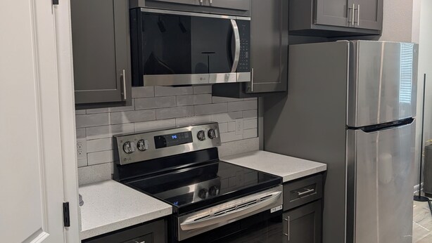 Une cuisine moderne avec des meubles gris, un réfrigérateur en acier inoxydable, un four et un four à micro-ondes.