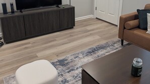 Un salon moderne avec un téléviseur à écran plat posé sur une console en bois foncé, un canapé en cuir marron, un pouf blanc et une table basse sur laquelle se trouve un pot de confiture.