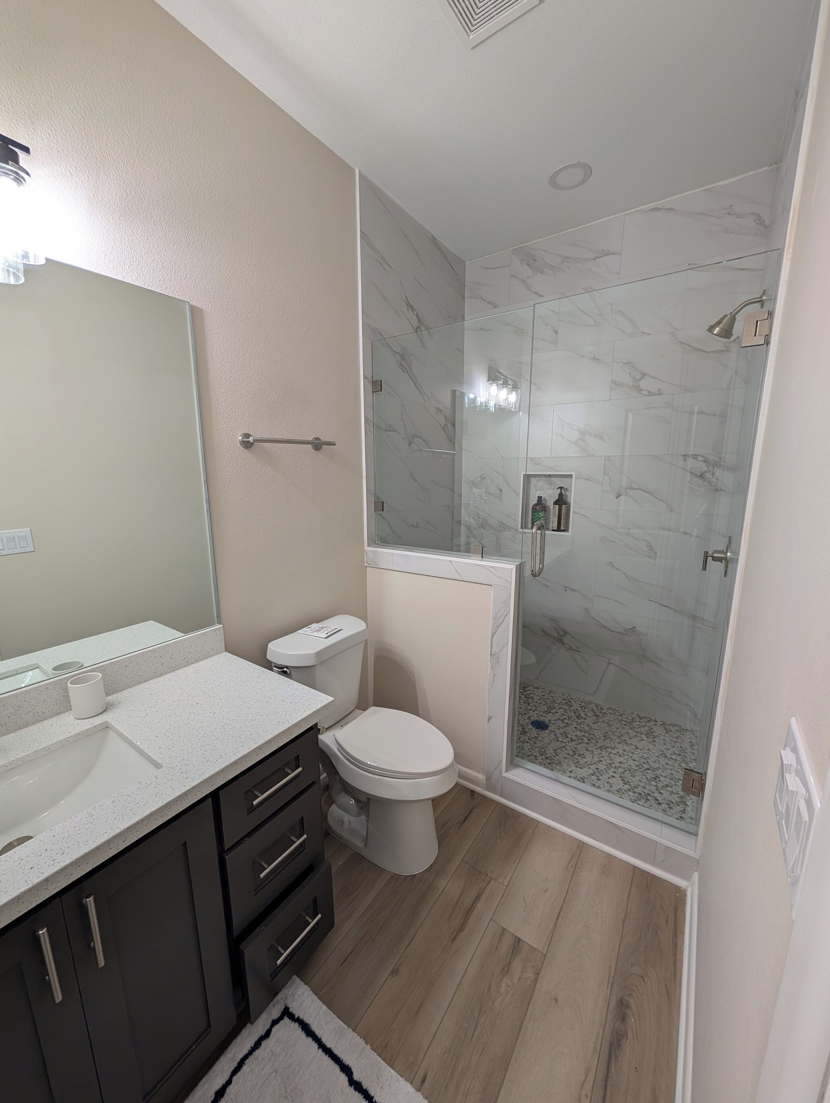 A modern bathroom with a glass-enclosed shower, a white toilet, and a vanity with a mirror and sink.
