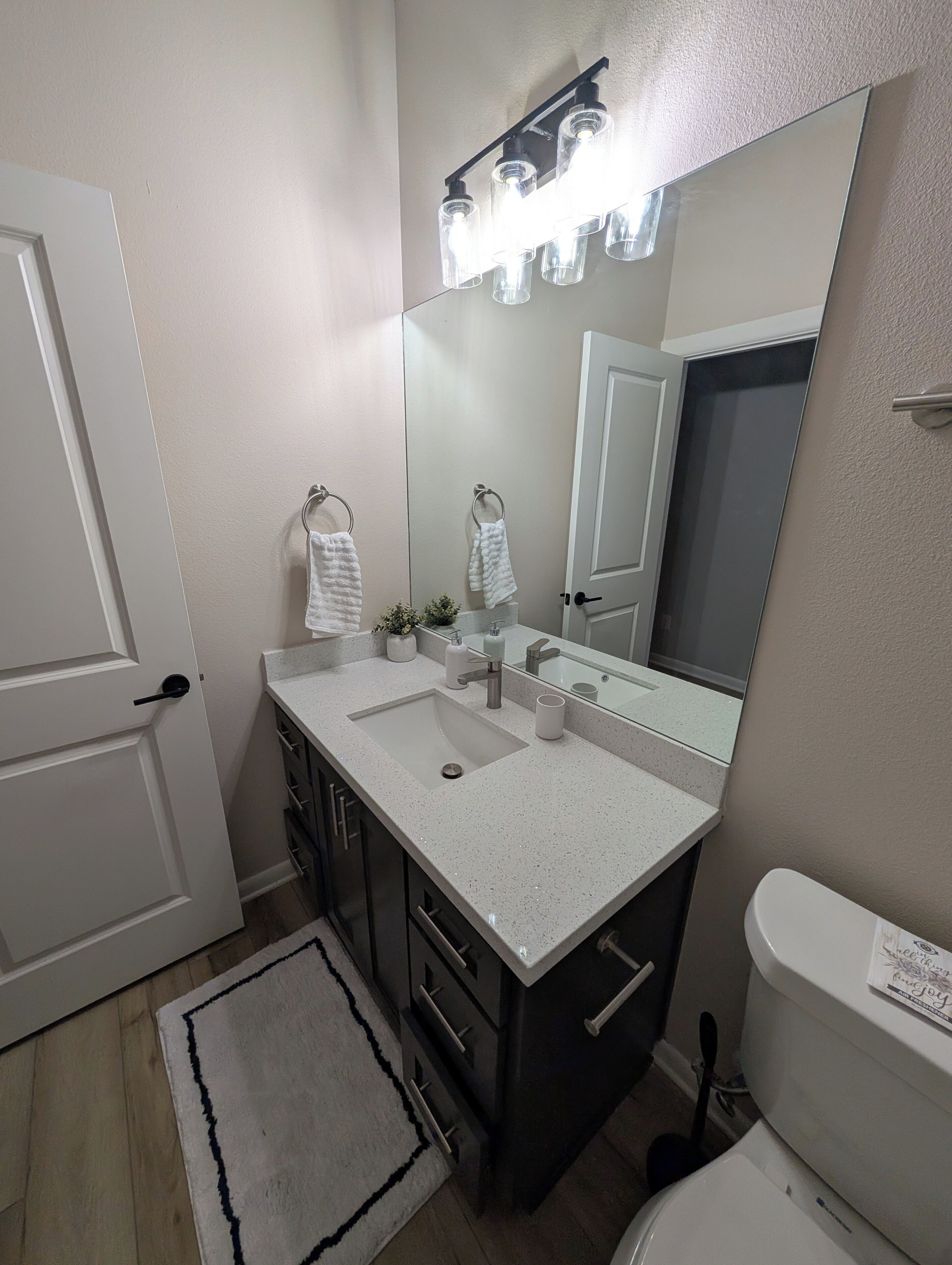 A bathroom with a white sink, dark cabinets, a large mirror, and a toilet.