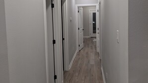 Un couloir aux murs blancs, au plancher en bois et aux portes blanches dotées de poignées noires.