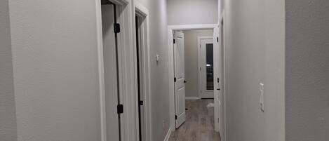 A hallway with white walls, wooden flooring, and white doors with black handles.