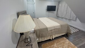 A bedroom with a bed, a lamp, a TV, and a door. - Nassau Hideaway: Steps away from the beach, Down Town, Cable Beach, PI & more.   (Nassau)