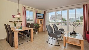 A modern living room with a dining area, large windows, and a TV. - Vacation home Angela 1 - Cozy vacation home in the countryside - with fireplace, garden & (Korswandt)
