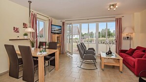 A modern living room with a dining area, a red sofa, a TV, and large windows. - Vacation home Angela 1 - Cozy vacation home in the countryside - with fireplace, garden & (Korswandt)