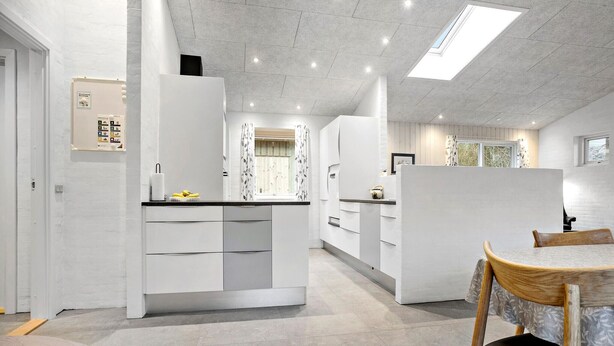 A modern kitchen with white cabinetry, a central island, and a dining area with a wooden table and chair.