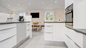 A modern kitchen with white cabinetry, a coffee maker, and a dining area with a table and chairs.