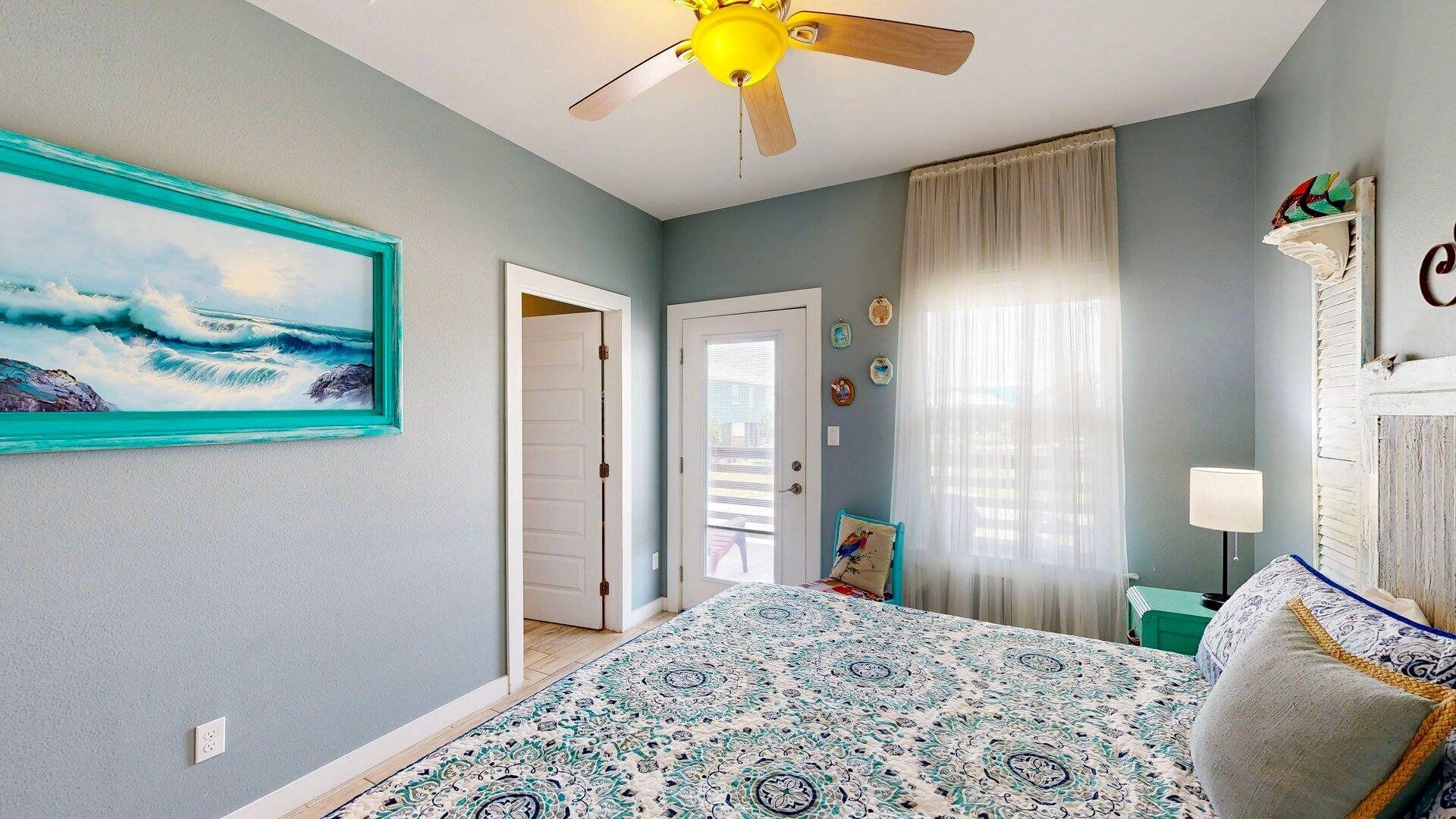 A bedroom with a bed, a ceiling fan, a window with curtains, and a painting on the wall.