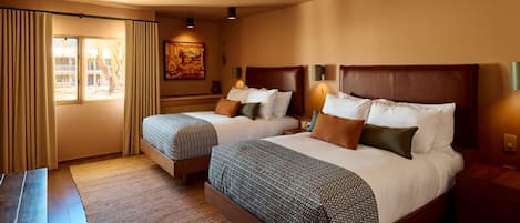 Een hotelkamer met twee bedden, een groot raam met gordijnen, een schilderij aan de muur en een houten vloer.