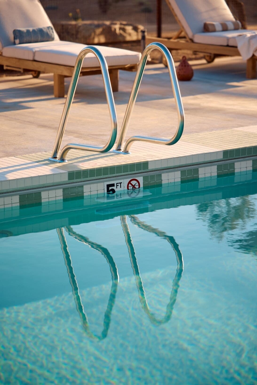 A poolside area with lounge chairs and a metal pool ladder.