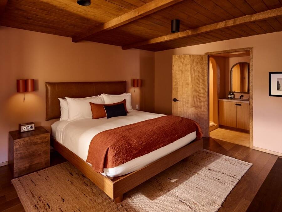 Un dormitorio con cama de madera, mesita de noche, alfombra grande y techo de madera.