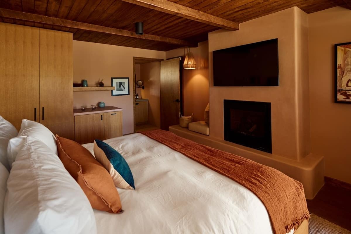 A bedroom with a large bed, wooden wardrobe, a fireplace, and a TV mounted on the wall.