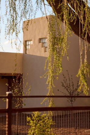 Un edificio de fachada plana y múltiples ventanas, rodeado de árboles y una valla.