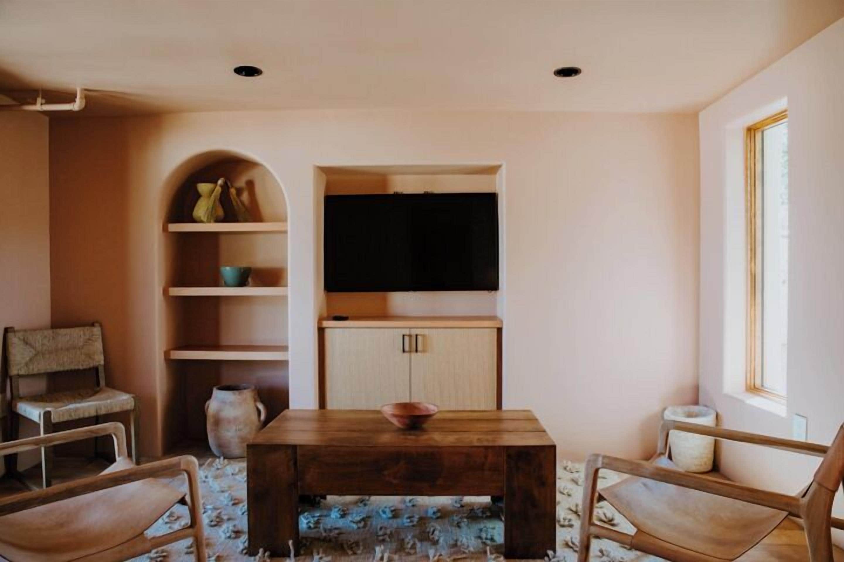 Un salón acogedor con una mesa de centro de madera, dos sillones, un televisor y estanterías empotradas.