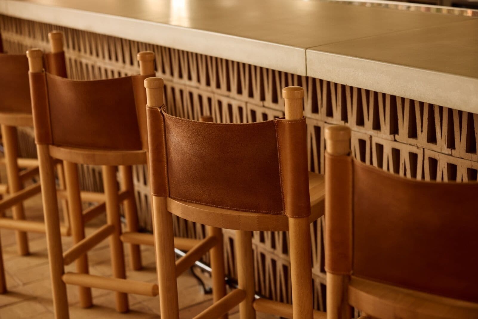 Une rangée de chaises en bois, dotées d’assises et de dossiers en cuir, est placée devant un comptoir, lequel est agrémenté d’un dossier à motifs.