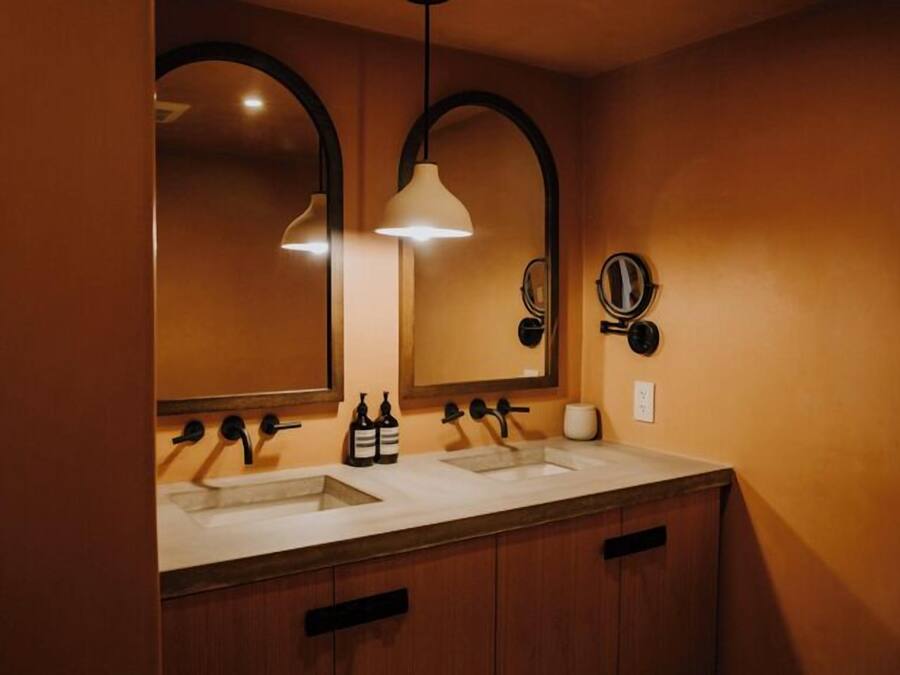 Un baño moderno con dos lavamanos, armarios de madera e iluminación colgante.