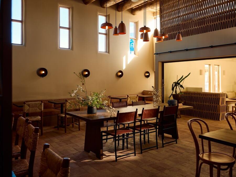 A cozy restaurant with wooden furniture, pendant lighting, and a large window providing natural light.